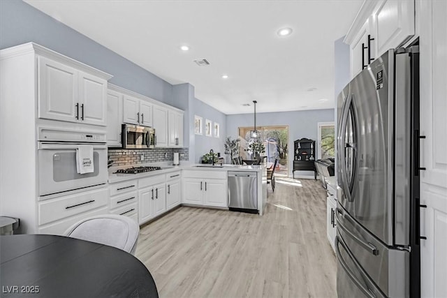 kitchen with decorative light fixtures, white cabinetry, tasteful backsplash, light hardwood / wood-style flooring, and appliances with stainless steel finishes