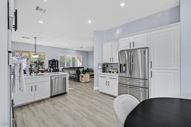 kitchen with sink, white cabinets, light hardwood / wood-style floors, pendant lighting, and appliances with stainless steel finishes