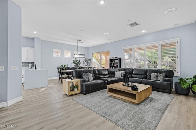 living room with an inviting chandelier, light hardwood / wood-style floors, and sink