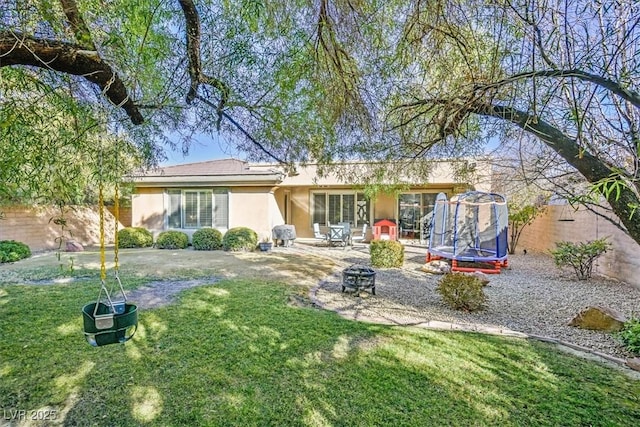 rear view of property with an outdoor fire pit, a yard, and a trampoline