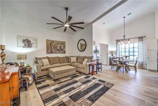 living room featuring ceiling fan with notable chandelier, lofted ceiling, and light wood-type flooring