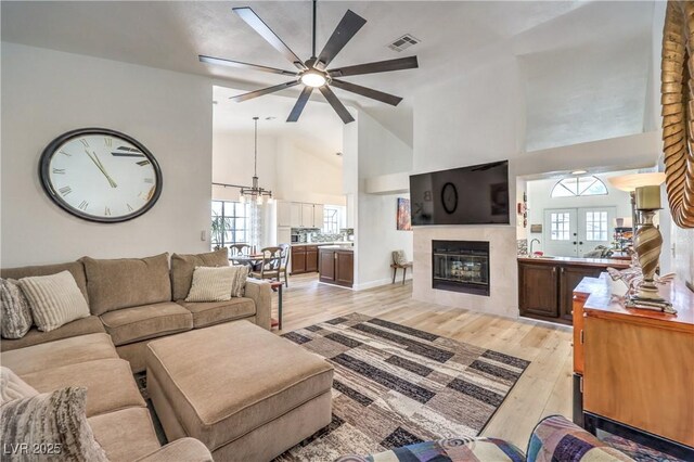 living room featuring a tiled fireplace, light hardwood / wood-style floors, high vaulted ceiling, sink, and ceiling fan with notable chandelier