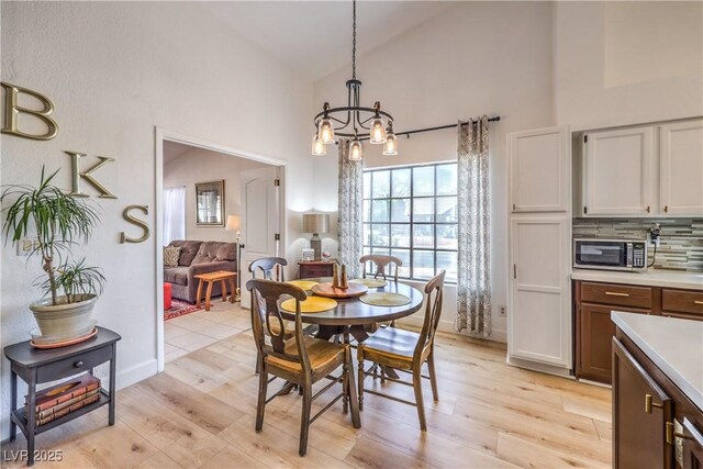 dining area with high vaulted ceiling, a chandelier, and light hardwood / wood-style flooring