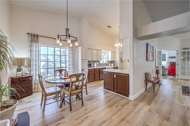 dining area with high vaulted ceiling, an inviting chandelier, and light hardwood / wood-style floors