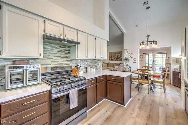 kitchen with kitchen peninsula, pendant lighting, gas stove, decorative backsplash, and white cabinetry