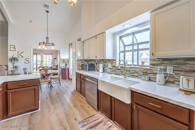 kitchen featuring sink, dishwasher, light wood-type flooring, pendant lighting, and a notable chandelier