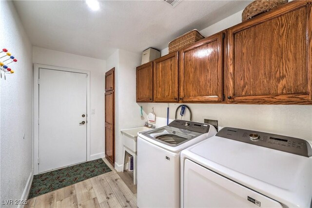 clothes washing area with washing machine and dryer, light wood-type flooring, and cabinets