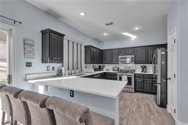 kitchen featuring light stone counters, stainless steel appliances, light hardwood / wood-style floors, a kitchen bar, and sink