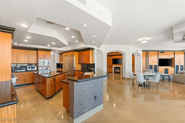 kitchen with stainless steel microwave, sink, kitchen peninsula, light tile patterned floors, and a center island with sink