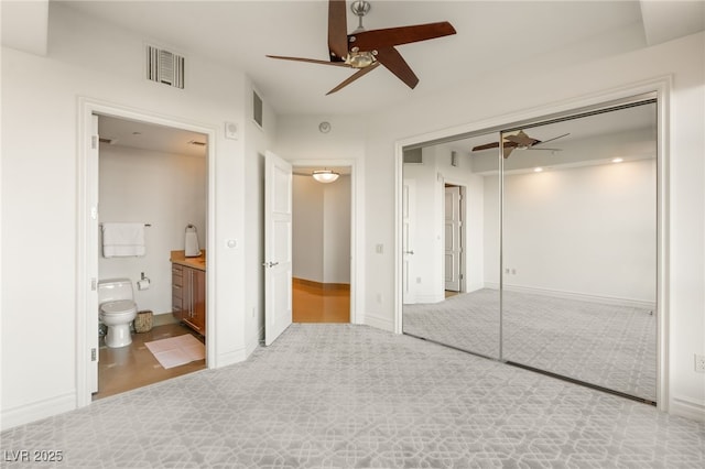 unfurnished bedroom featuring light carpet, a closet, connected bathroom, and ceiling fan