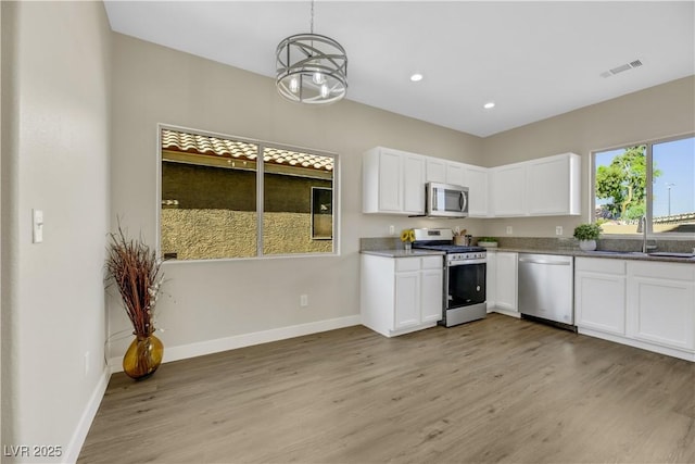 kitchen featuring decorative light fixtures, stainless steel appliances, light hardwood / wood-style floors, white cabinetry, and sink