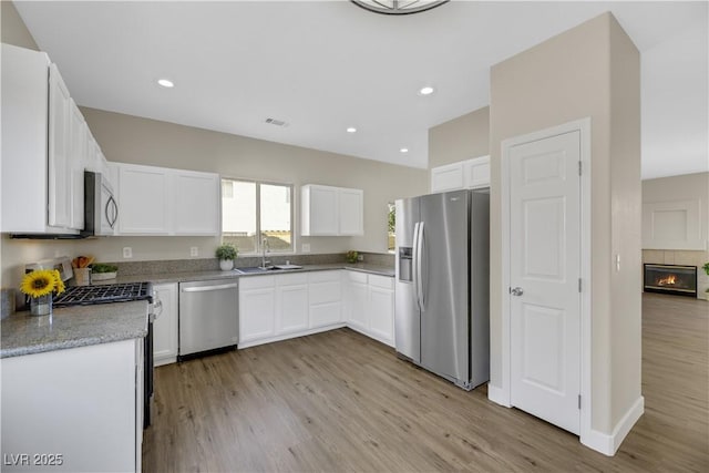 kitchen with stainless steel appliances, white cabinetry, a tile fireplace, and sink