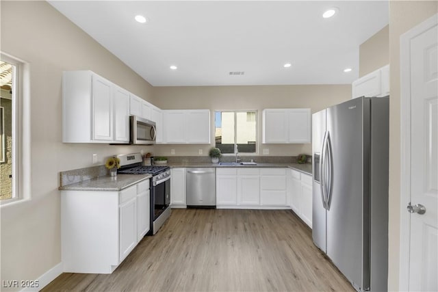 kitchen with light stone counters, light wood-type flooring, white cabinetry, appliances with stainless steel finishes, and sink