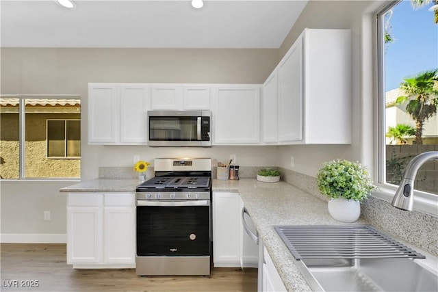 kitchen with stainless steel appliances, sink, white cabinetry, light hardwood / wood-style flooring, and light stone countertops