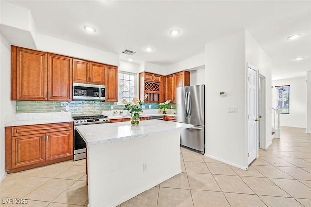 kitchen featuring stainless steel appliances, a center island, light tile patterned floors, and light stone counters