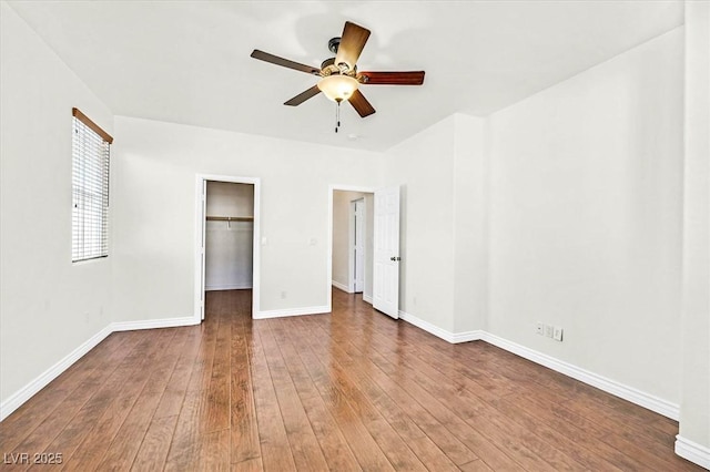 unfurnished bedroom with ceiling fan, a spacious closet, a closet, and hardwood / wood-style flooring