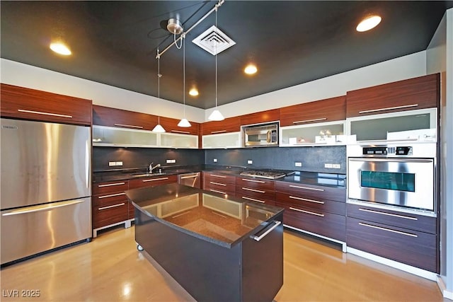 kitchen with appliances with stainless steel finishes, pendant lighting, a kitchen island, sink, and tasteful backsplash