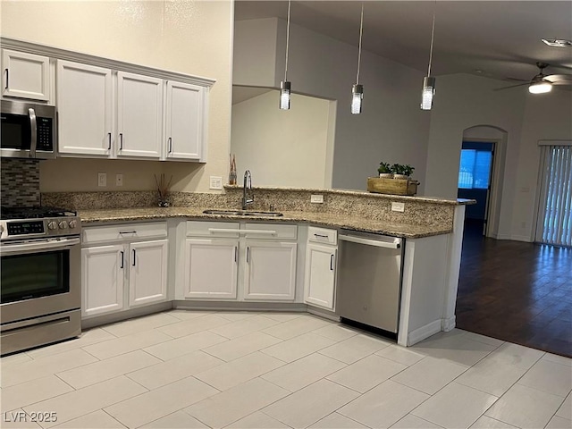 kitchen featuring stainless steel appliances, kitchen peninsula, pendant lighting, sink, and stone countertops