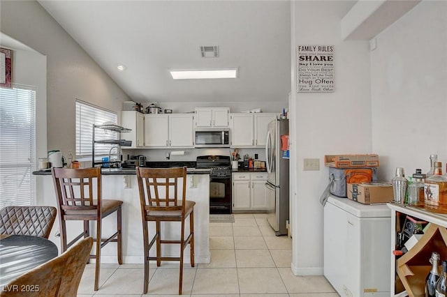 kitchen featuring appliances with stainless steel finishes, white cabinets, vaulted ceiling, and a breakfast bar area