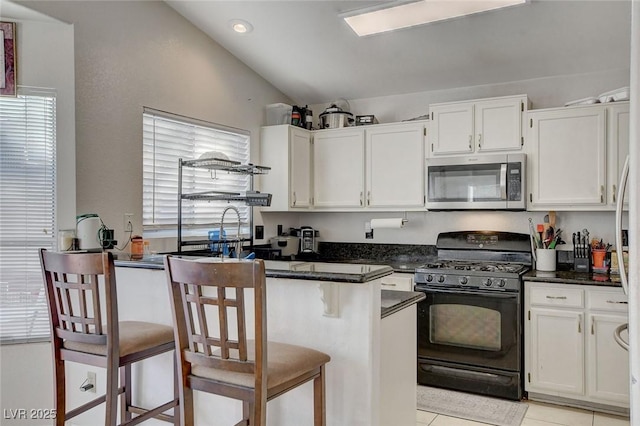 kitchen with white cabinets, vaulted ceiling, black gas range oven, and a kitchen bar