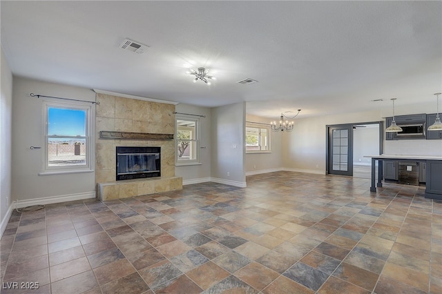 unfurnished living room featuring a healthy amount of sunlight, a tiled fireplace, and a chandelier