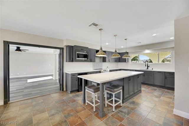 kitchen featuring stainless steel microwave, ceiling fan, a kitchen island, a kitchen bar, and sink