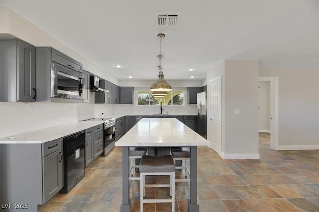 kitchen with wall chimney exhaust hood, stainless steel appliances, decorative backsplash, sink, and gray cabinetry