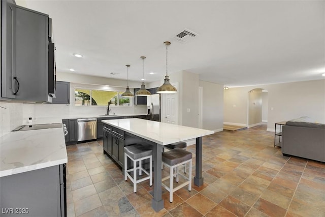 kitchen with stainless steel appliances, gray cabinetry, decorative light fixtures, a kitchen breakfast bar, and a center island