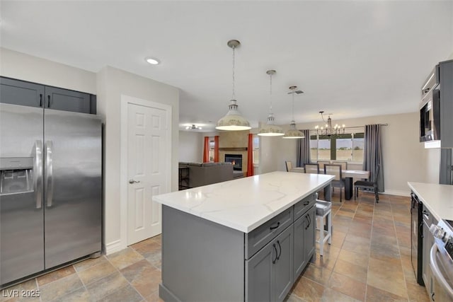 kitchen with appliances with stainless steel finishes, a notable chandelier, hanging light fixtures, a kitchen island, and light stone counters