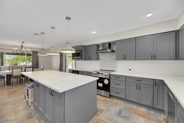 kitchen with pendant lighting, appliances with stainless steel finishes, a kitchen island, wall chimney range hood, and gray cabinetry