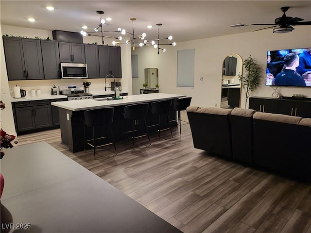 kitchen with sink, a kitchen island with sink, dark wood-type flooring, a breakfast bar area, and stainless steel appliances