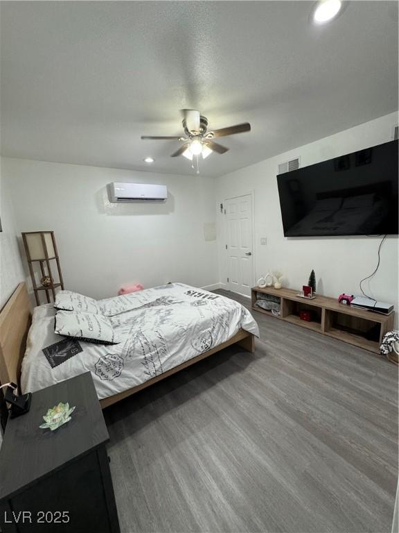 bedroom with dark hardwood / wood-style floors, ceiling fan, and a wall mounted AC