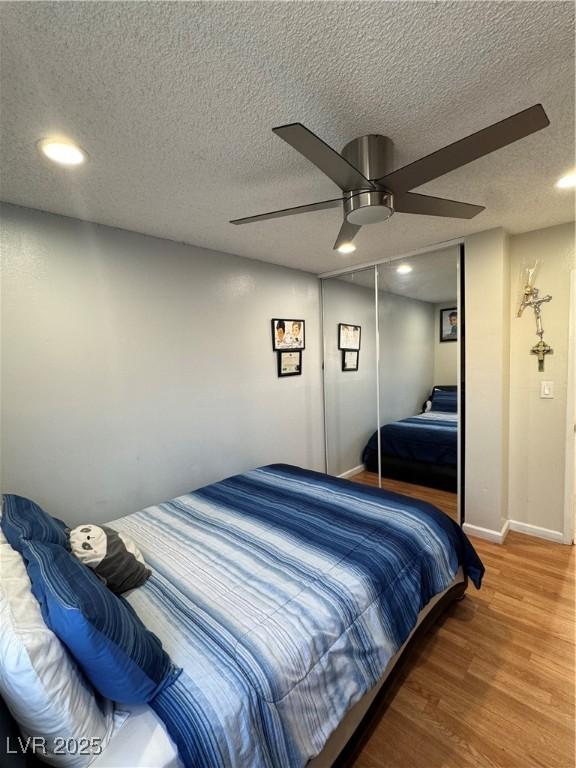 bedroom with hardwood / wood-style flooring, a textured ceiling, ceiling fan, and a closet