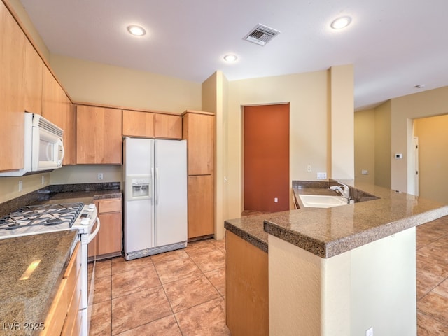 kitchen with kitchen peninsula, white appliances, light tile patterned flooring, light brown cabinetry, and sink