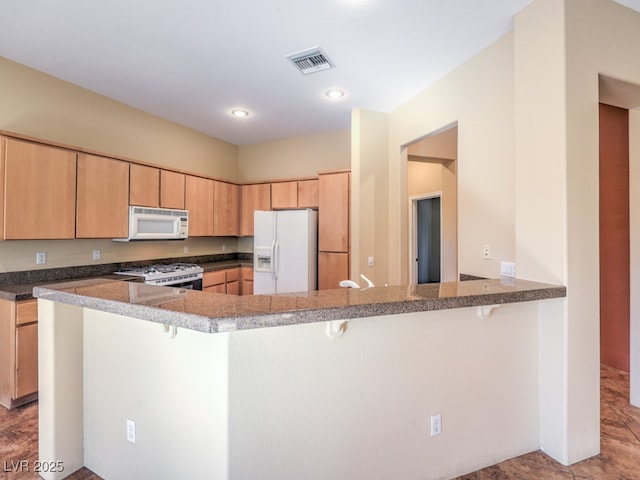 kitchen featuring light brown cabinetry, white appliances, kitchen peninsula, and a breakfast bar area