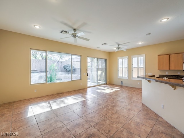 interior space featuring a kitchen breakfast bar, ceiling fan, light tile patterned flooring, and light brown cabinetry