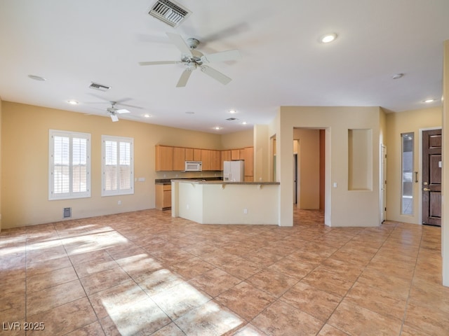 kitchen with light tile patterned floors, ceiling fan, light brown cabinets, white appliances, and a kitchen breakfast bar