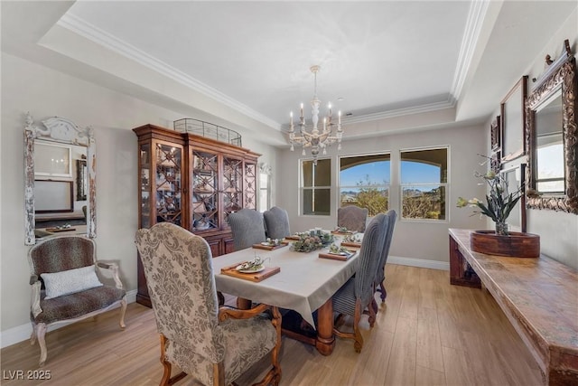 dining room featuring a tray ceiling, light hardwood / wood-style flooring, ornamental molding, and a notable chandelier