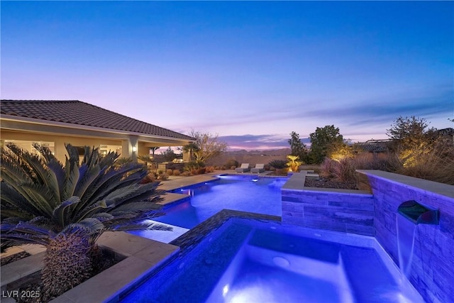 pool at dusk with pool water feature and an in ground hot tub