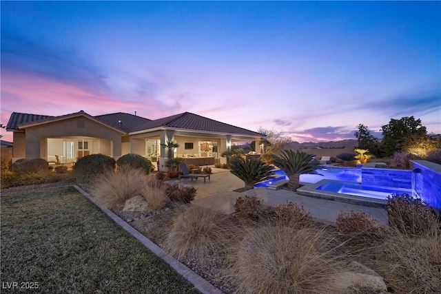 back house at dusk with a patio area and a swimming pool with hot tub