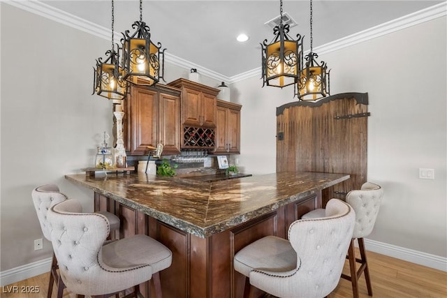 bar with decorative light fixtures, light wood-type flooring, dark stone countertops, and ornamental molding