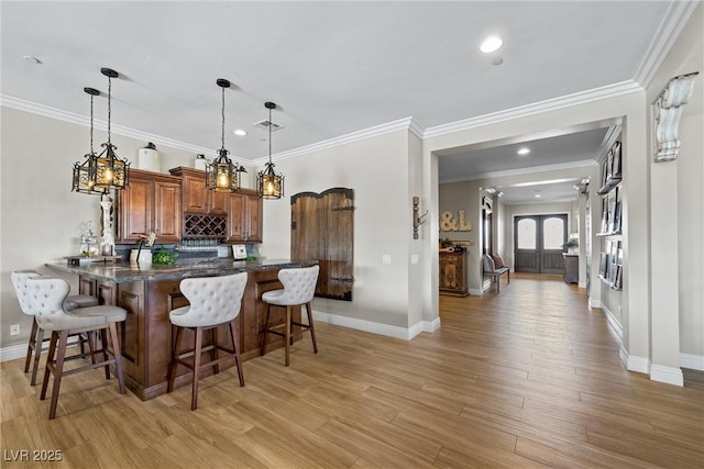 kitchen with a breakfast bar, kitchen peninsula, light hardwood / wood-style flooring, hanging light fixtures, and ornamental molding