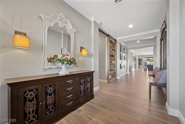 hallway featuring light wood-type flooring, ornamental molding, and a barn door