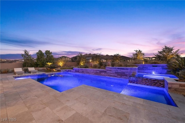 pool at dusk with pool water feature, an in ground hot tub, and a patio