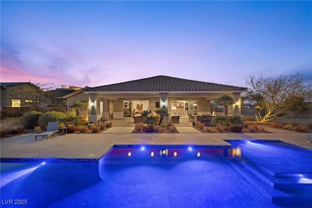 pool at dusk with a hot tub and a patio