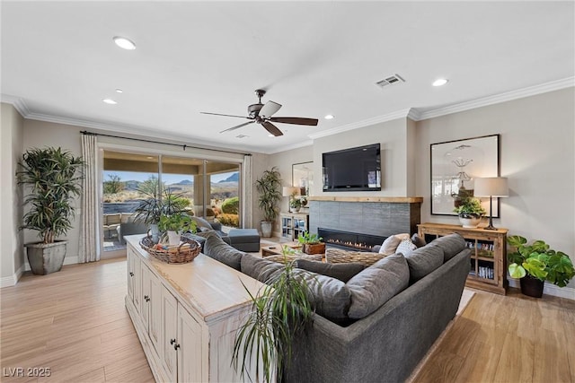 living room featuring ceiling fan, a fireplace, ornamental molding, and light hardwood / wood-style floors