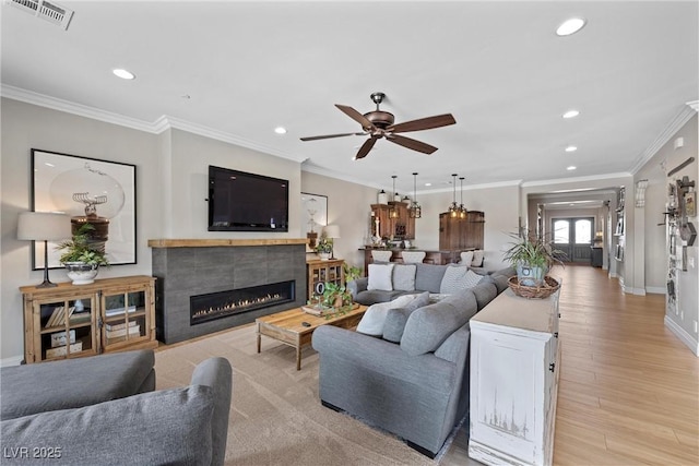 living room with ceiling fan, ornamental molding, light hardwood / wood-style flooring, and a tiled fireplace