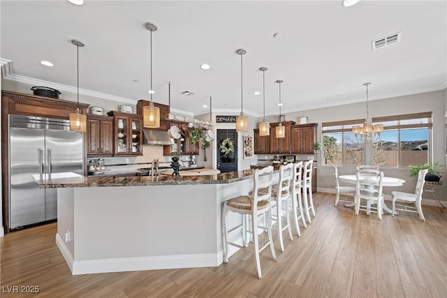 kitchen featuring built in fridge, decorative light fixtures, and dark stone countertops