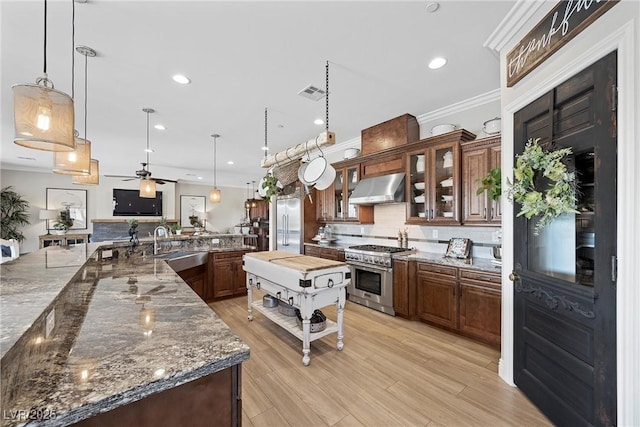 kitchen featuring premium appliances, ceiling fan, decorative light fixtures, dark stone counters, and wall chimney range hood