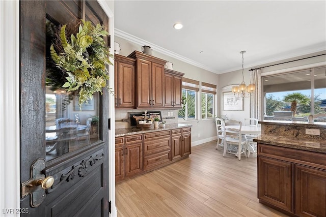 kitchen featuring tasteful backsplash, hanging light fixtures, light wood-type flooring, ornamental molding, and dark stone counters